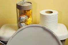 a toilet with two rolls of toilet paper next to it and a jar filled with candy