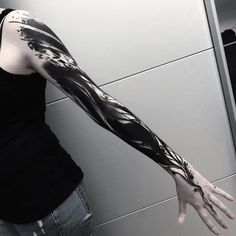 a woman with her arm covered in black and white ink is standing next to a wall