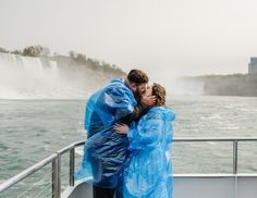 a man and woman kissing on a boat in front of the niagara falls with raincoats over their faces