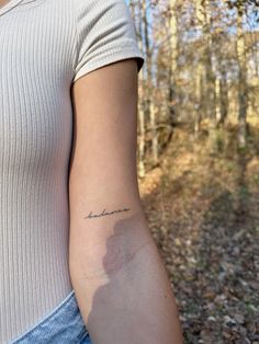 a woman with a small tattoo on her left arm in the middle of a forest