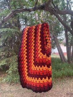 an orange and red crocheted blanket hanging from a tree in front of some trees