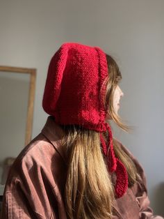 a woman wearing a red knitted hat with a bow on her head and long blonde hair