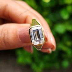 a person's hand holding a gold ring with an emerald colored stone in it