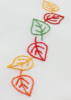 an embroidered piece with leaves on it is shown in red, green, yellow and orange