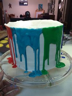 the cake is decorated with multicolored icing and has dripping paint on it