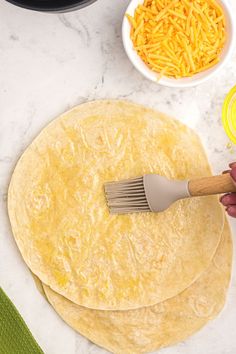 two tortillas with cheese being spread on top