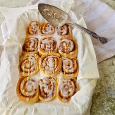 cinnamon rolls with icing sitting on top of a white plate next to a spoon