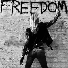 a woman standing in front of a brick wall with the word freedom written on it