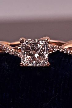 an engagement ring with a princess cut diamond in the center on a black velvet surface