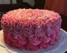 a large pink cake sitting on top of a white plate covered in frosting flowers