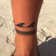 a woman's foot with a wave tattoo on her left leg and the ocean in the background