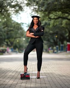 a woman in a black suit and hat posing for the camera with her arms crossed