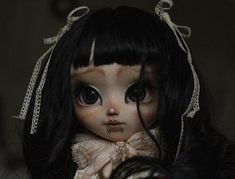 a doll with long black hair and big eyes wearing a white dress, holding her hands to her face