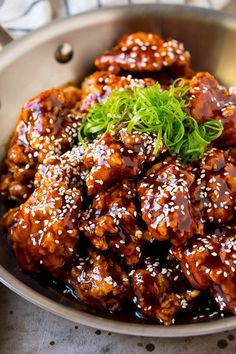 a bowl filled with meat covered in sesame seeds and garnished with green herbs