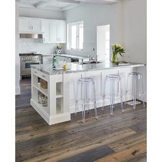 a large kitchen with white cabinets and counter tops, along with two bar stools