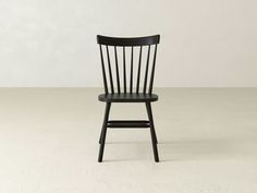 a black wooden chair sitting on top of a white floor next to a gray wall