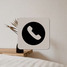 a phone sign sitting on top of a wooden shelf next to a plant in a vase