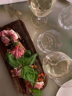 a table topped with wine glasses and plates filled with food next to each other on top of a wooden cutting board