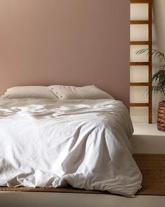 a bed with white linens and pillows in a room next to a plant on the floor