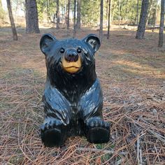 a statue of a bear sitting in the middle of a forest with pine needles on the ground