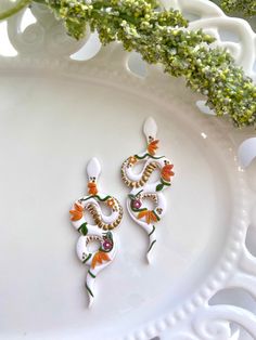 two pairs of white and orange earrings sitting on top of a white plate next to flowers