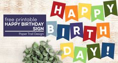 a happy birthday sign with green leaves and flowers on a white wooden background, surrounded by bunting flags