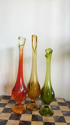 three different colored vases sitting on top of a checkered table