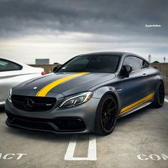 two cars parked side by side in a parking lot with dark clouds above them and one has yellow stripes on the hood