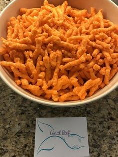 a bowl filled with cheetos sitting on top of a counter next to a note