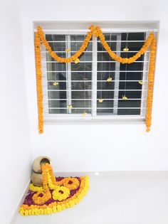 an arrangement of flowers and garlands in front of a window with a vase on the floor