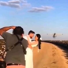 a man and woman standing on the side of a road next to an airplane flying in the sky