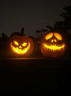 two jack o lantern pumpkins lit up in the dark with faces carved into them