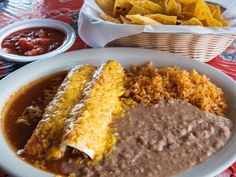 mexican food with beans, rice and tortillas on a tablecloth next to bowls of salsa