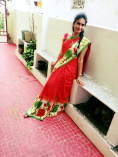 a woman in a red and green sari sitting on a white bench next to plants