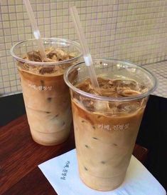 two iced coffees sitting on top of a table next to each other with straws in them