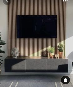 a flat screen tv mounted to the side of a wall next to potted plants