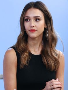 a woman with long hair wearing a black dress and holding her hands on her chest