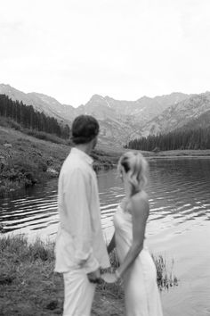 a man and woman standing next to each other in front of a lake