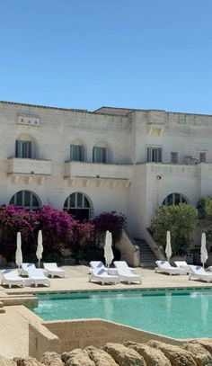 an outdoor swimming pool with lounge chairs and umbrellas in front of a large building