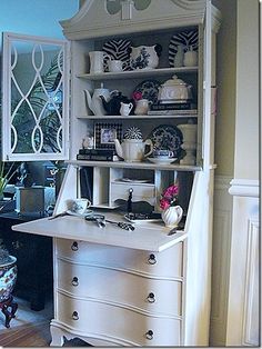 a white china cabinet in a living room next to a chair and table with vases on it