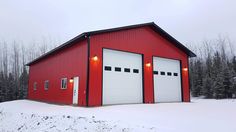 a red building with two garage doors and windows on top of snow covered ground in front of trees