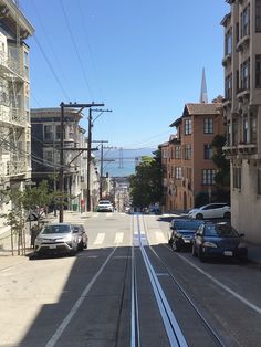 cars parked on the side of a road next to tall buildings and power lines with water in the background