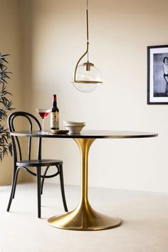 a dining room table with two chairs and a wine bottle on it, next to a plant