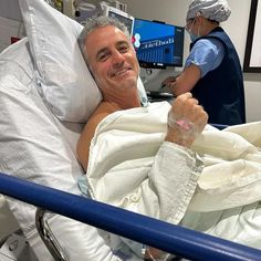 a man laying in a hospital bed with his arm wrapped around him and smiling at the camera