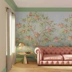 a pink couch sitting in front of a wall with flowers painted on it and a lamp next to it