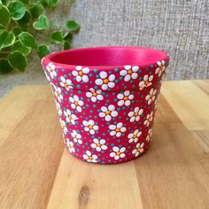 a pink and white flower pot sitting on top of a wooden table next to a green plant