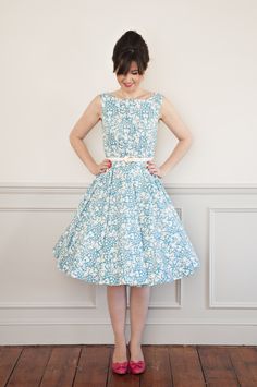 a woman standing in front of a wall wearing a blue dress with white flowers on it