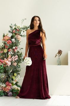 a woman in a long dress standing next to a flower arrangement and holding a bouquet