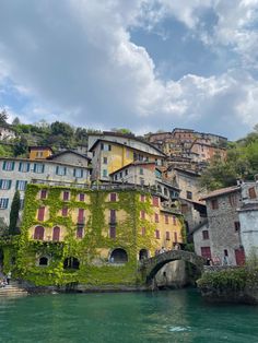 an old building with vines growing on it's side next to the water in front of some buildings