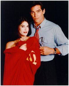 a man standing next to a woman holding a superman shirt on her chest and looking at the camera